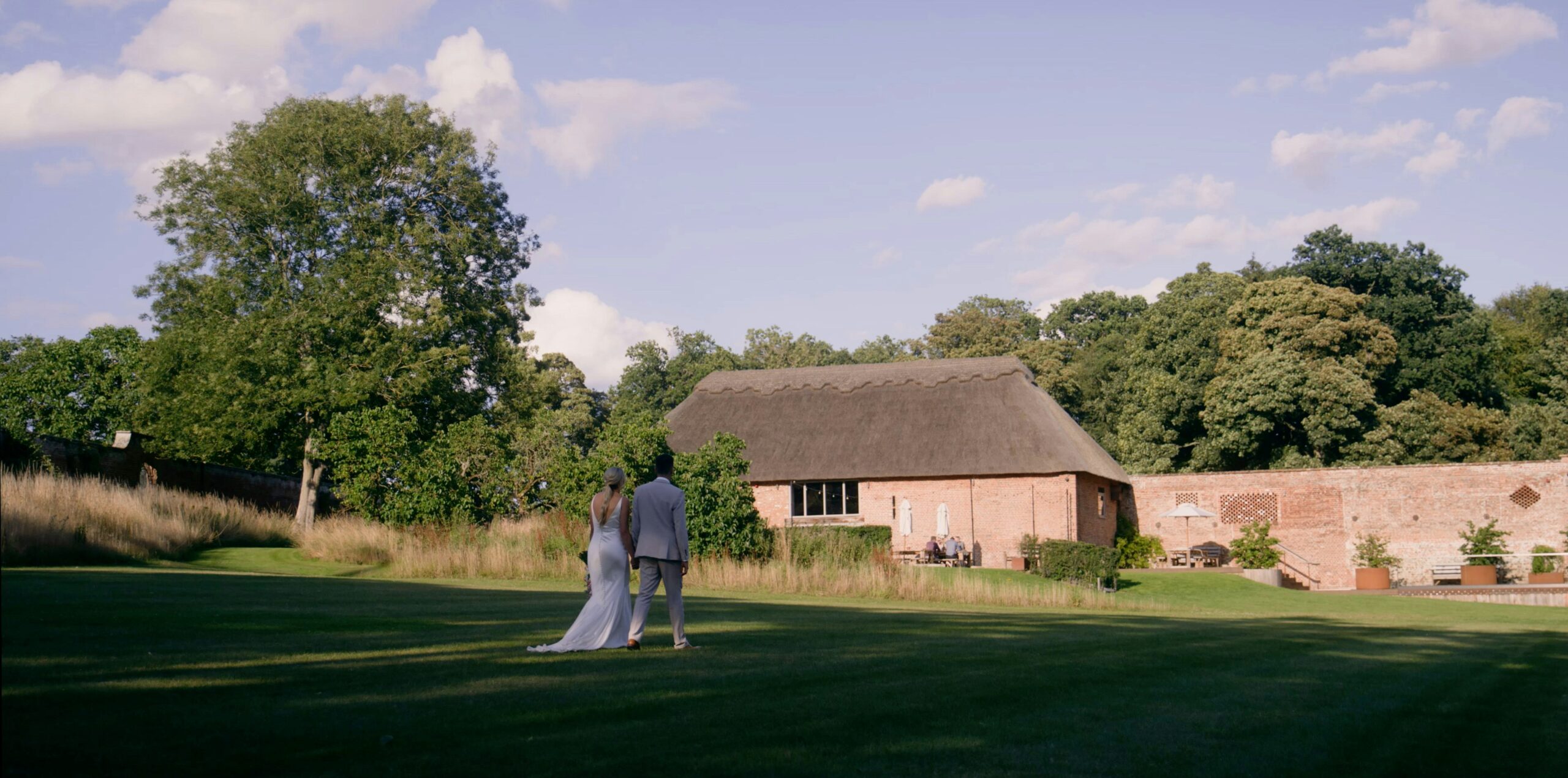 A still of a bride and groom walking towards a wedding venue in Norfolk.